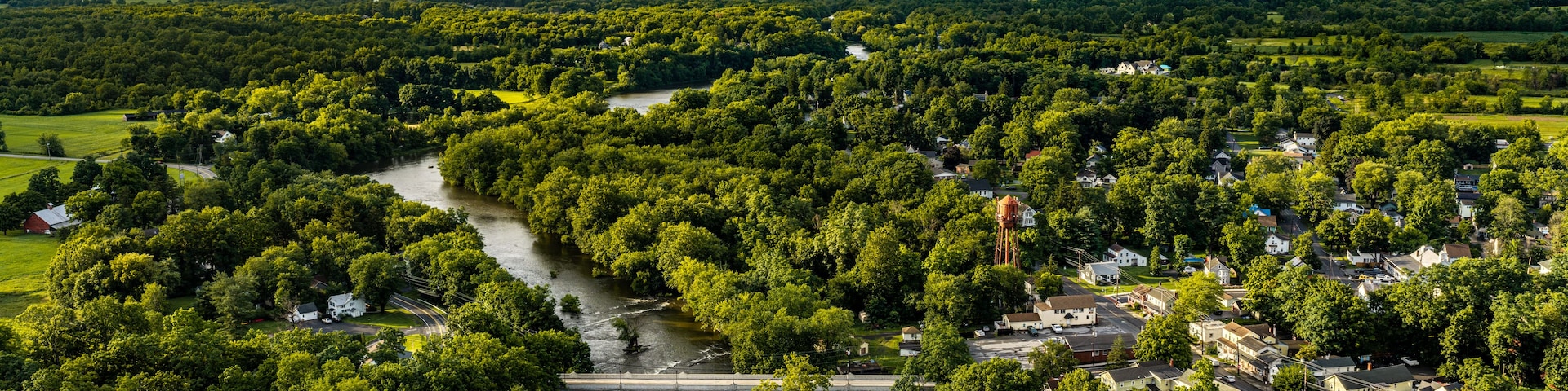 A river winding through a densely wooded area with a bridge and a small town.