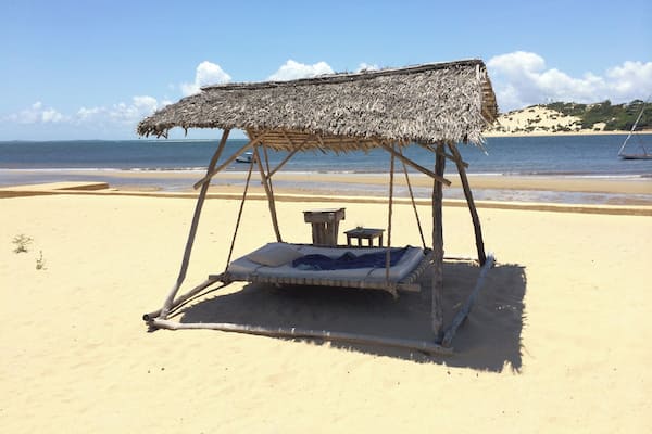 A beach with a thatched-roof swing bed.