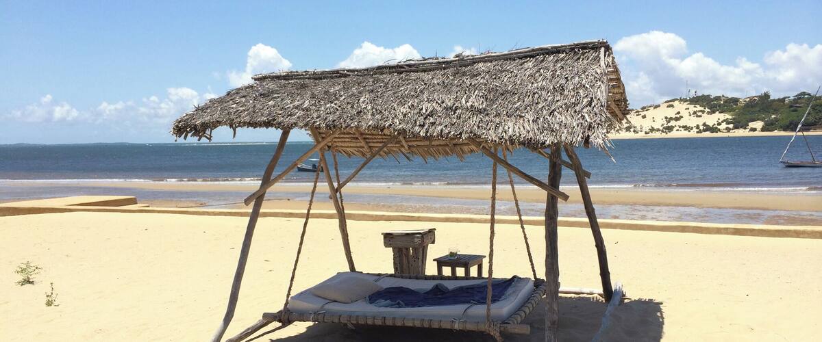 A beach with a thatched-roof swing bed.