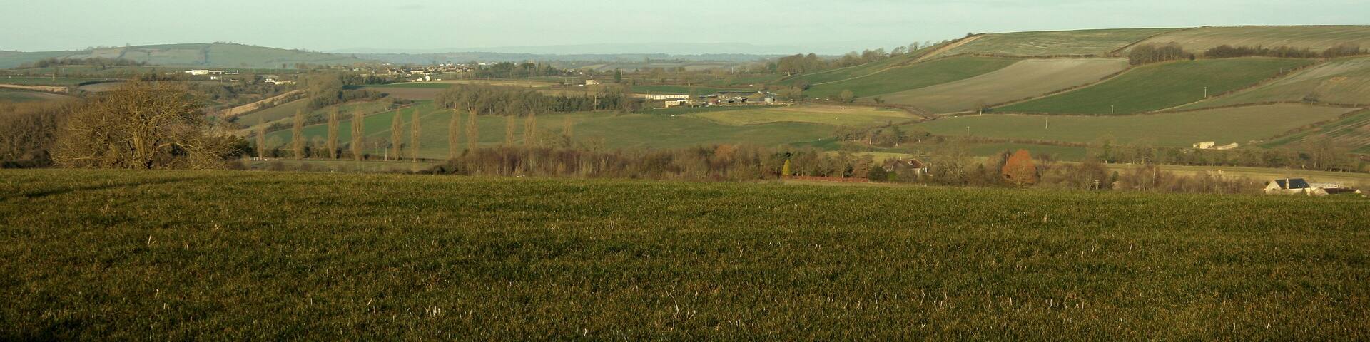 View north west from Tunley Road As much a question of what you don't see. Priston hides in the valley beyond the foreground field, just showing a few rooftops, Stanton Prior hides behind the prominent hill on the right. However, all is not lost, away near the left hand edge a small white rectangle marks the garage at the junction of the A39 and the A368 and a little to the right of it Marksbury appears with the top of its church tower showing above the trees (can be seen in the original). Still moving right and nearer the camera we fine Priston New Farm. Bits of Bristol are way beyond Marksbury but I won't tease you with that.