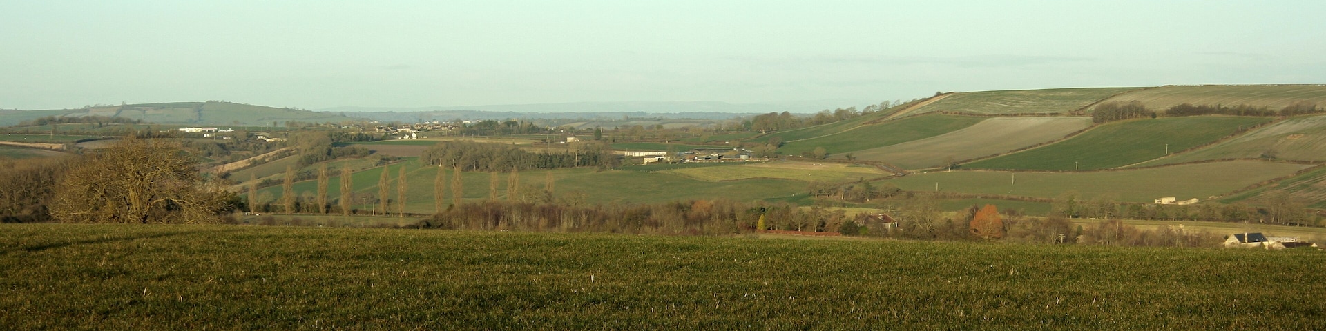 View north west from Tunley Road As much a question of what you don't see. Priston hides in the valley beyond the foreground field, just showing a few rooftops, Stanton Prior hides behind the prominent hill on the right. However, all is not lost, away near the left hand edge a small white rectangle marks the garage at the junction of the A39 and the A368 and a little to the right of it Marksbury appears with the top of its church tower showing above the trees (can be seen in the original). Still moving right and nearer the camera we fine Priston New Farm. Bits of Bristol are way beyond Marksbury but I won't tease you with that.
