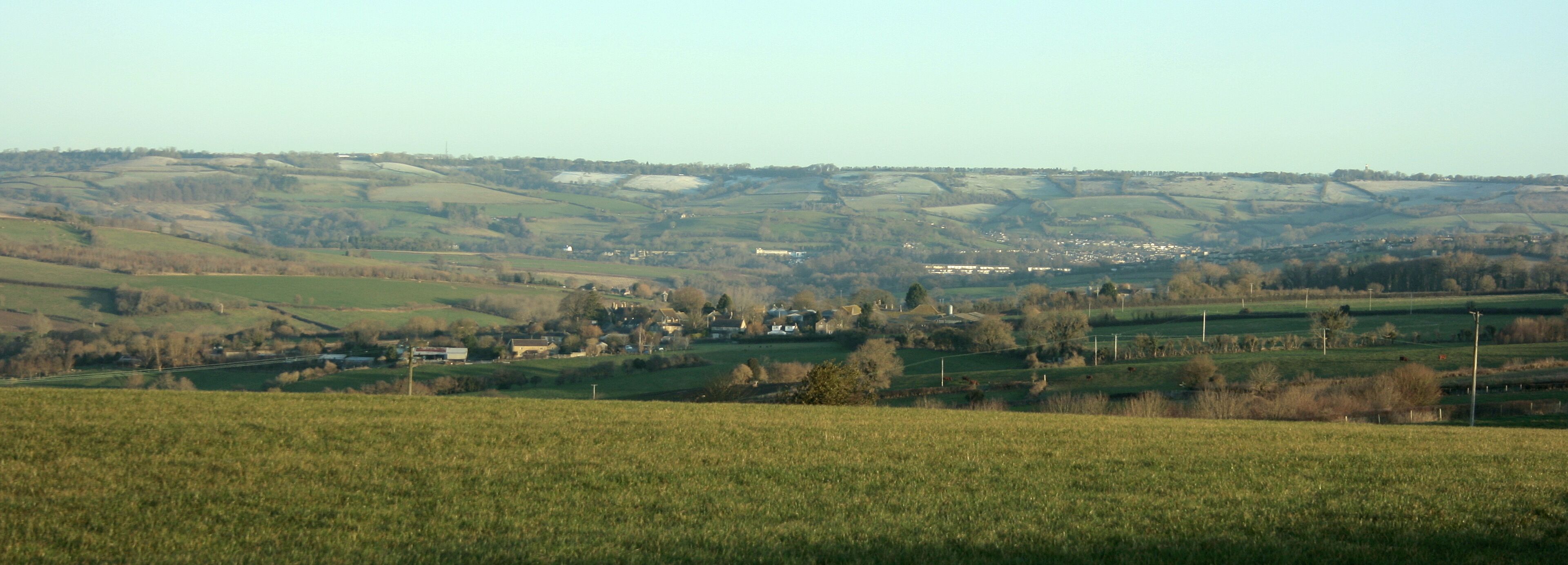East of north from Tunley Road As it approaches Tunley from the east the B3115 follows the top of a ridge giving views to the north and south on a clear day. Here we look north to Lansdown, the racecourse is just beyond the horizon. If you are looking for Kelston Round Hill it is dead centre frame well camouflaged against the background, its clump of trees only just clears the skyline. ST7167 Upper Weston is beneath Lansdown Hill to the right and nearer the camera we find bits of Inglesbatch and Priston.