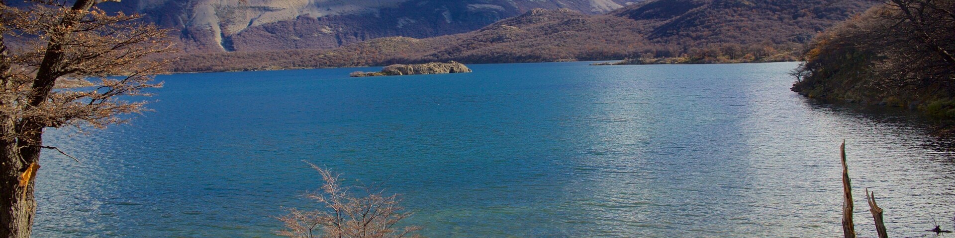 Un lago rodeado de montañas, con dos personas sentadas sobre rocas cerca de la orilla.