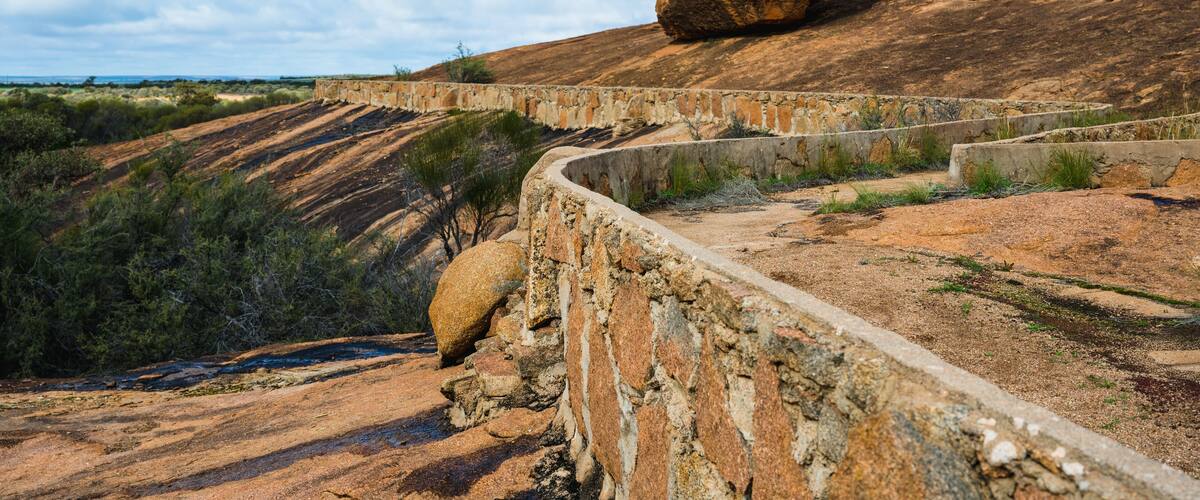 A stone bridge with a large boulder on top, surrounded by a hilly landscape.