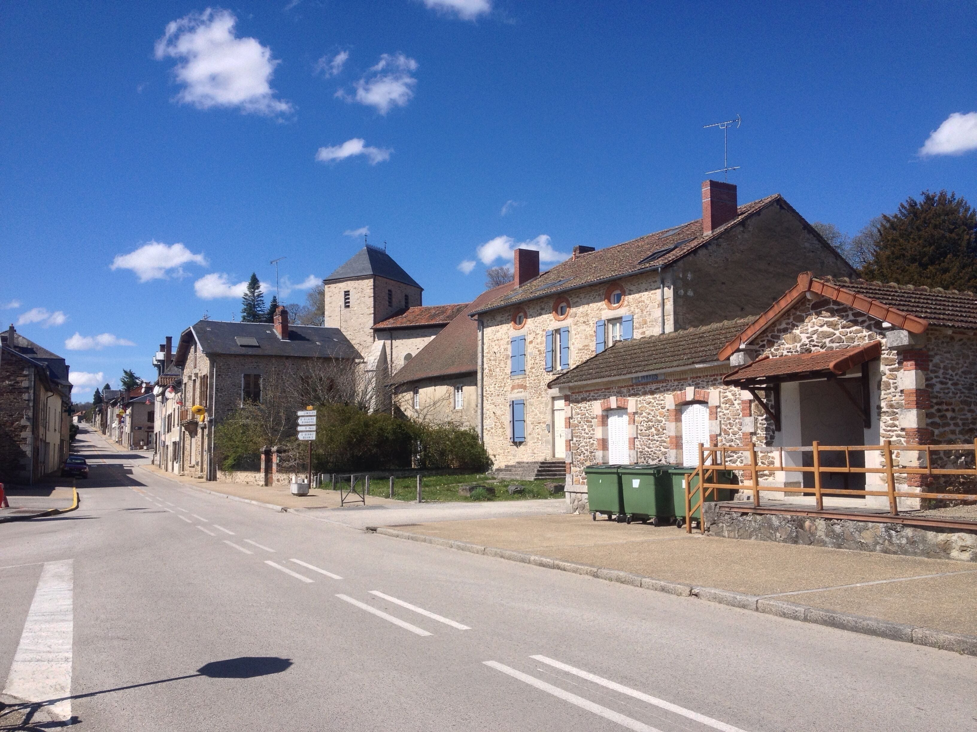 A quiet street lined with historic stone buildings, a clear blue sky, and a distant tower.