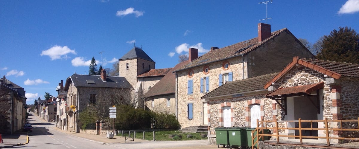 A quiet street lined with historic stone buildings, a clear blue sky, and a distant tower.