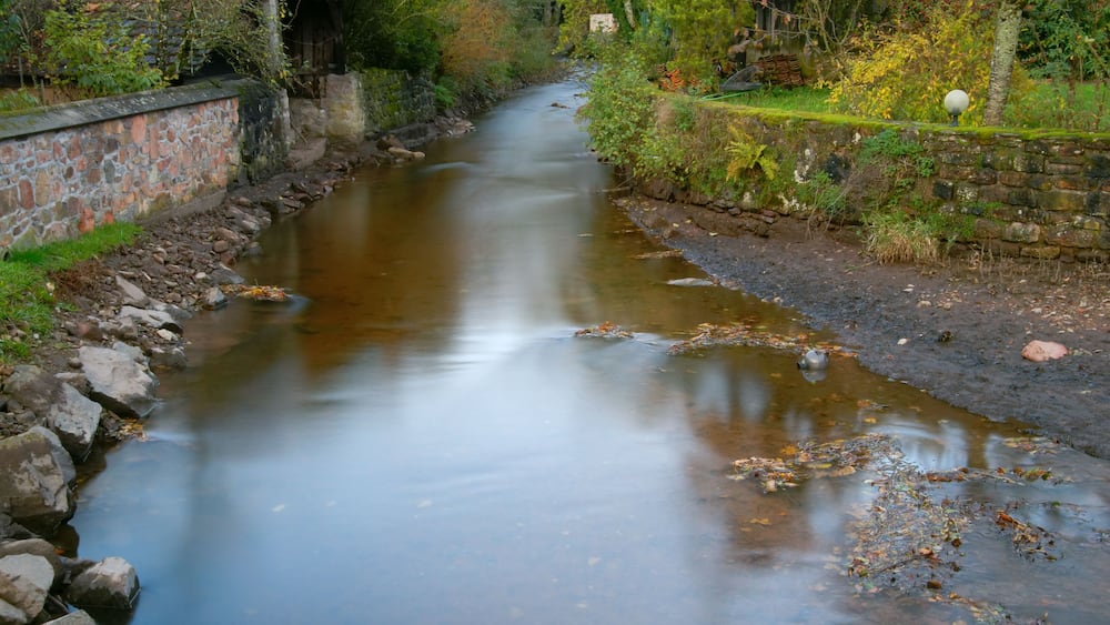 Une rivière paisible, bordée d’un côté par un mur de pierres et de l’autre par une structure en bois.