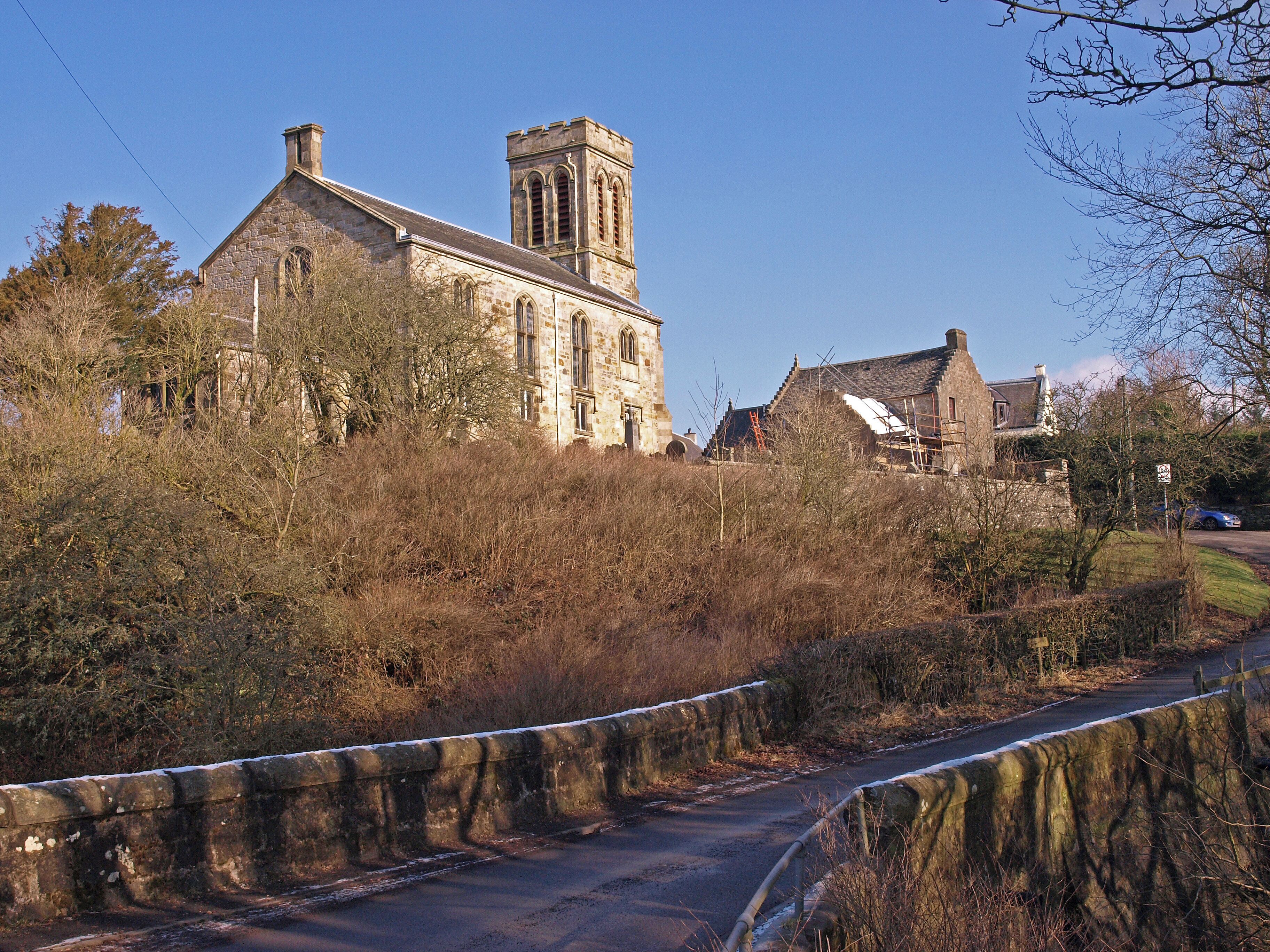 A stone church with a tower, surrounded by trees and a stone wall.