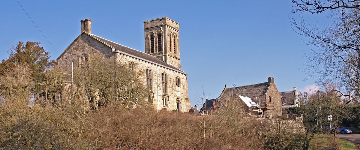 A stone church with a tower, surrounded by trees and a stone wall.