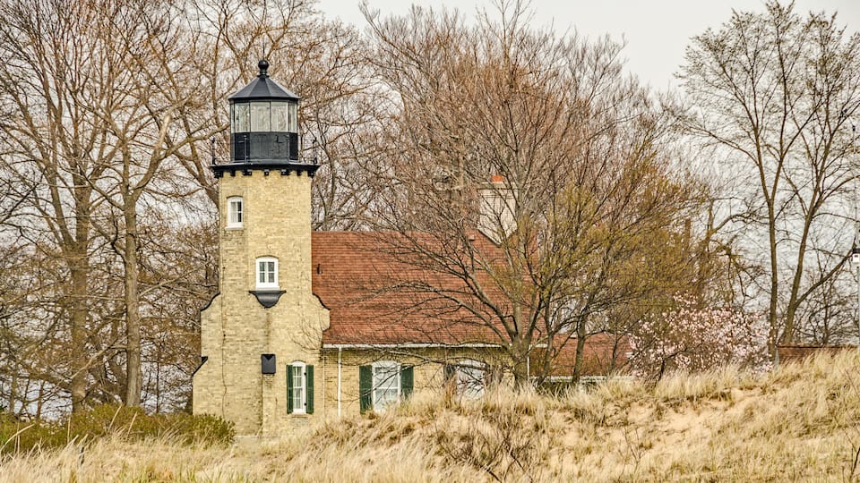 A lighthouse with a red roof, a tower with a black lantern room, and a building with green shutters.