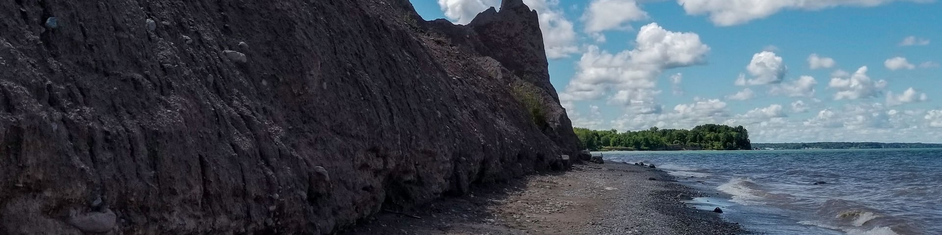 A rocky shoreline with a clear sky and scattered clouds.