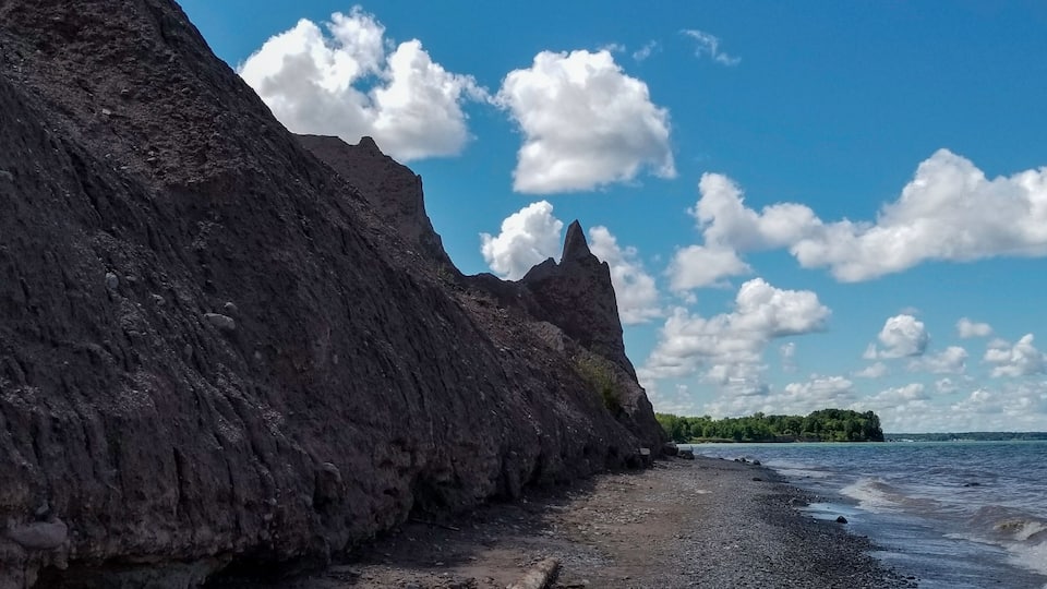 A rocky shoreline with a clear sky and scattered clouds.