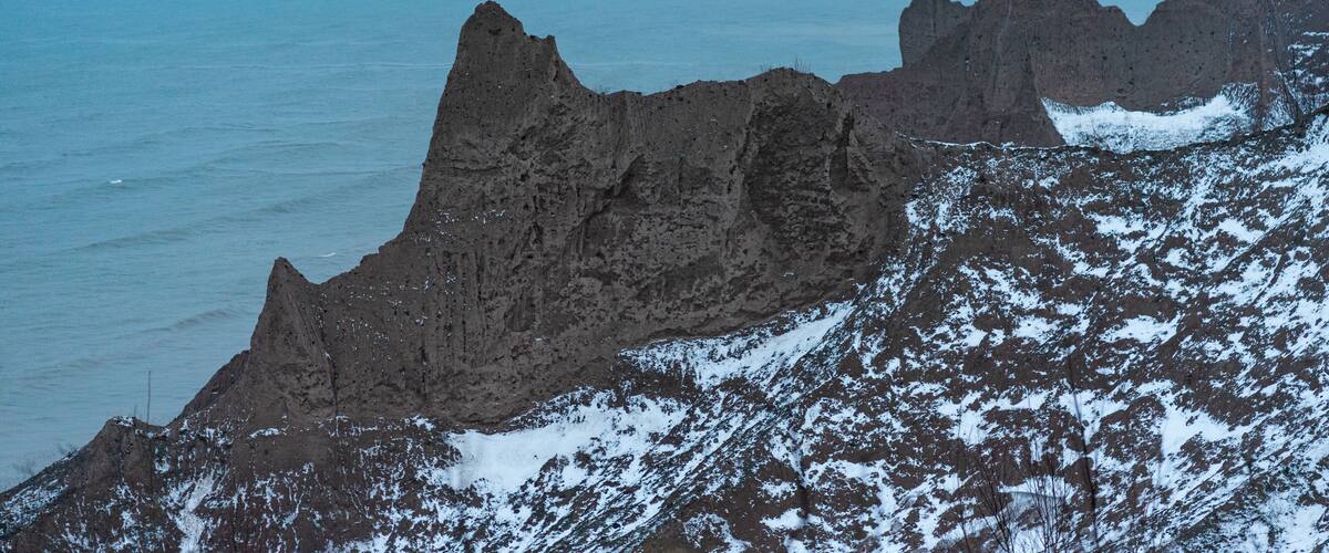 A rugged coastline with sharp rock formations and snow patches.