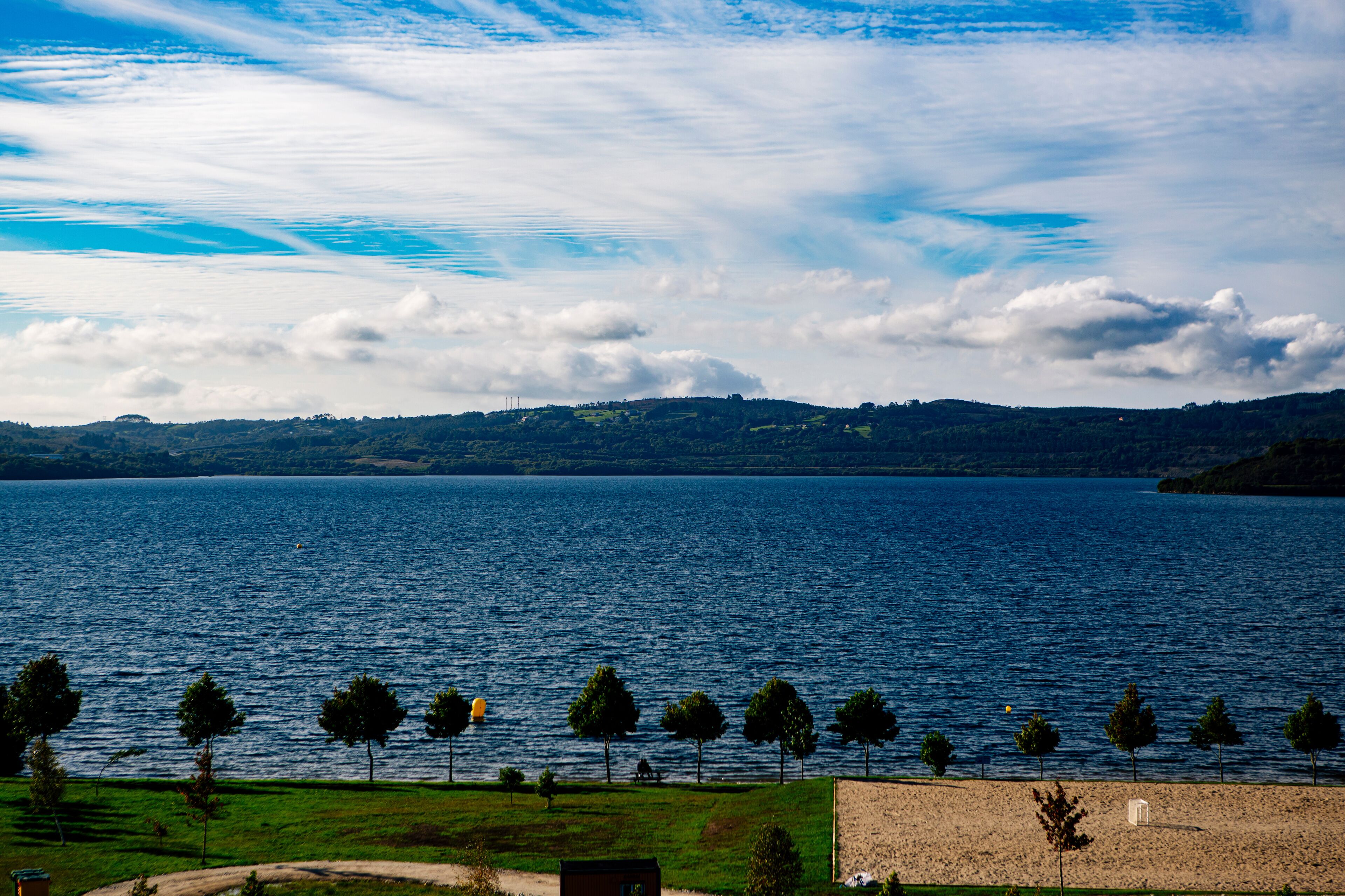A lake with a clear sky, trees, and distant hills.