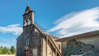 A stone church with a bell tower and a mural on the adjacent wall.