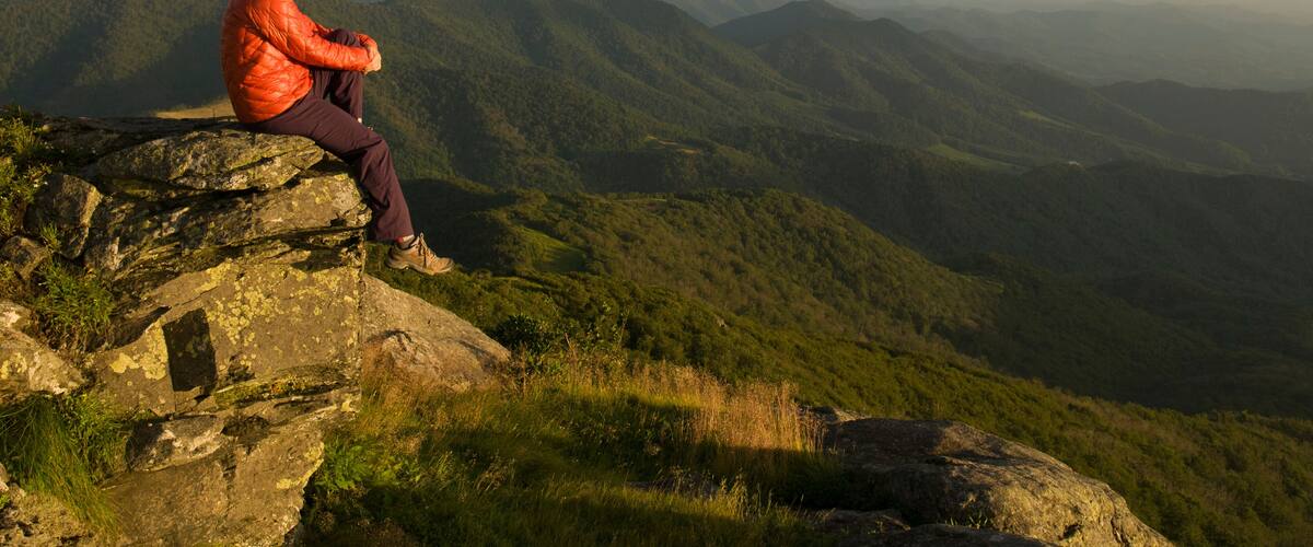 Une personne assise sur un rocher, avec un paysage montagneux en arrière-plan.