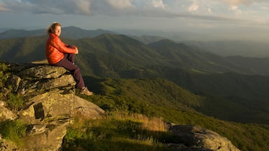 Uma pessoa sentada sobre uma rocha, com uma paisagem montanhosa ao fundo.