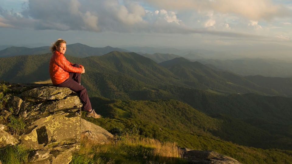 A person sitting on a rock with a mountainous landscape in the background.