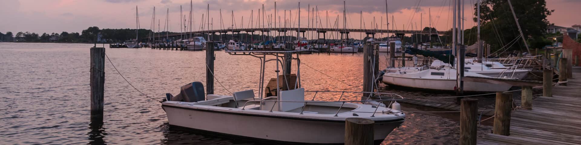 A marina with boats docked at wooden piers during sunset.