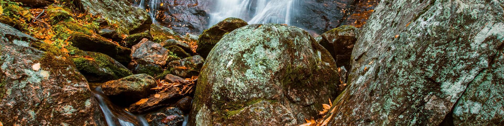 A waterfall cascading over rocks in a forest with autumn foliage.