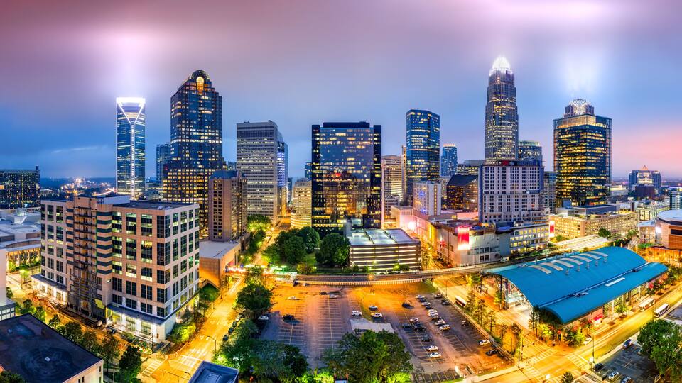 A cityscape at dusk with illuminated skyscrapers and a parking lot.