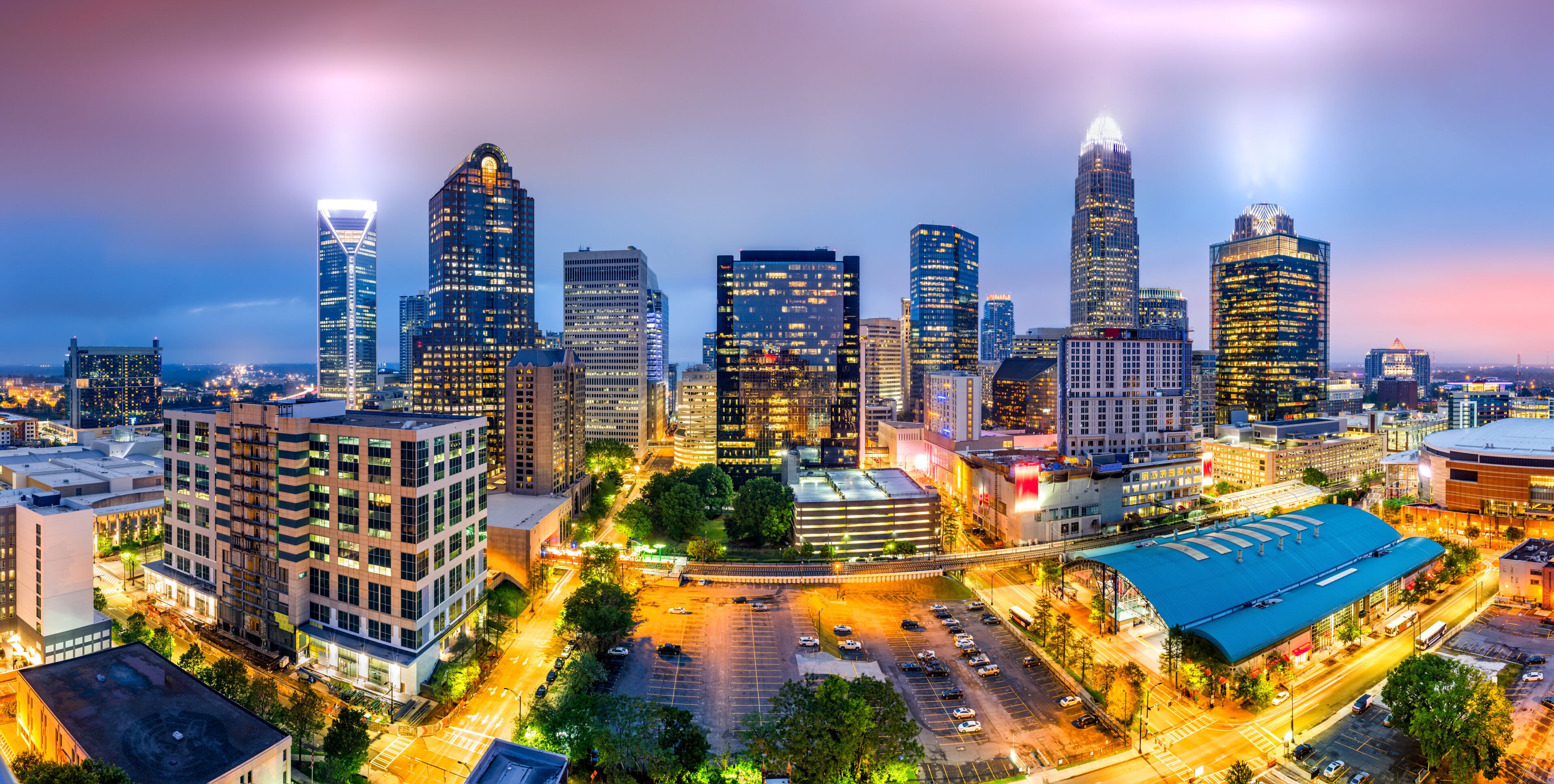 A cityscape at dusk with illuminated skyscrapers and a parking lot.