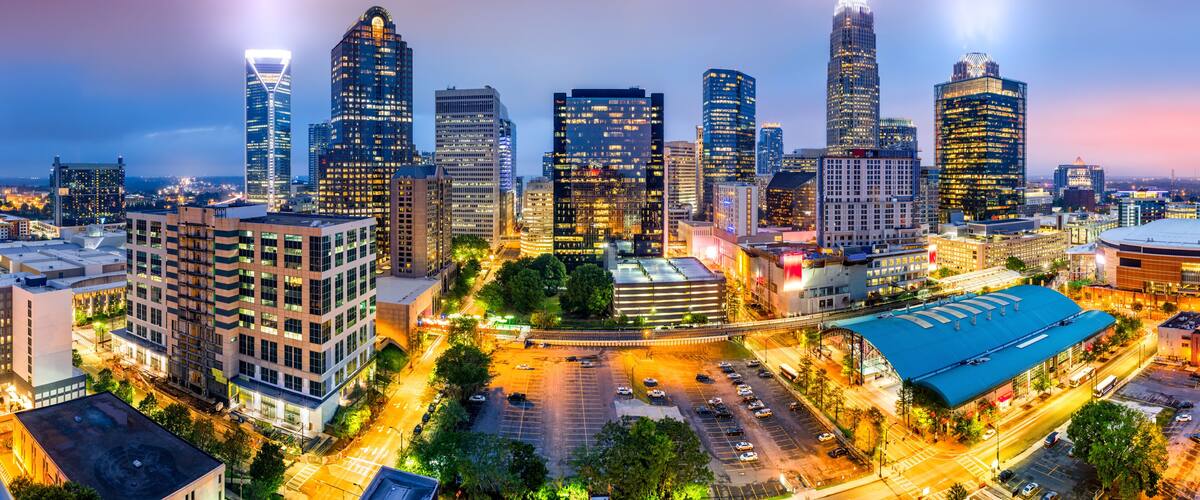 A cityscape at dusk with illuminated skyscrapers and a parking lot.