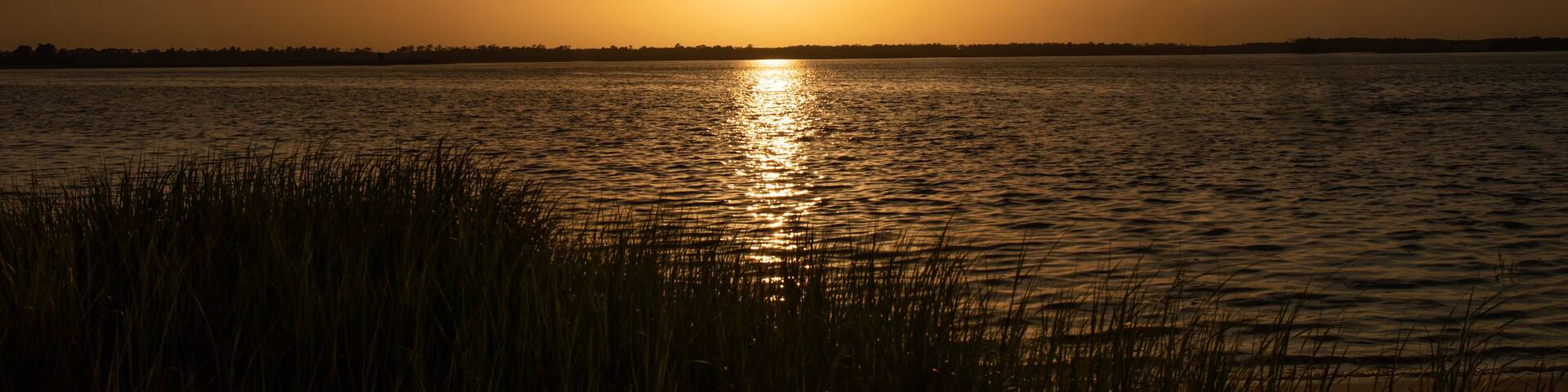A sunset over a calm body of water with grass in the foreground.
