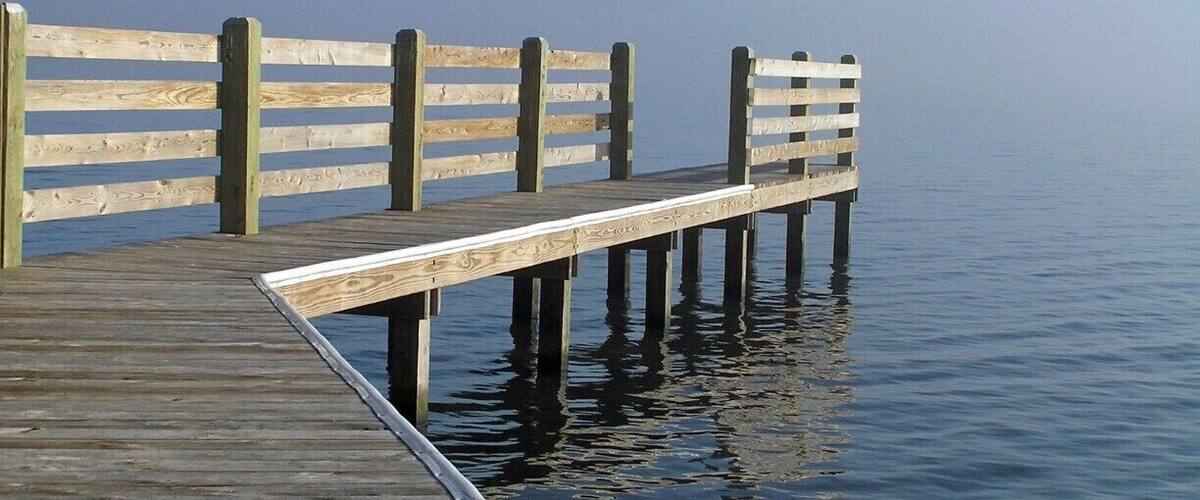 A wooden pier extending into calm water with a railing on one side.