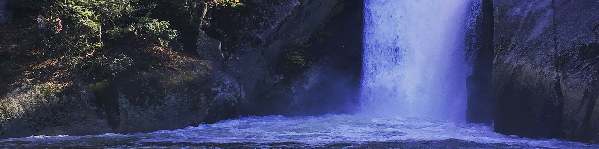 A waterfall cascading over rocks into a river surrounded by trees.