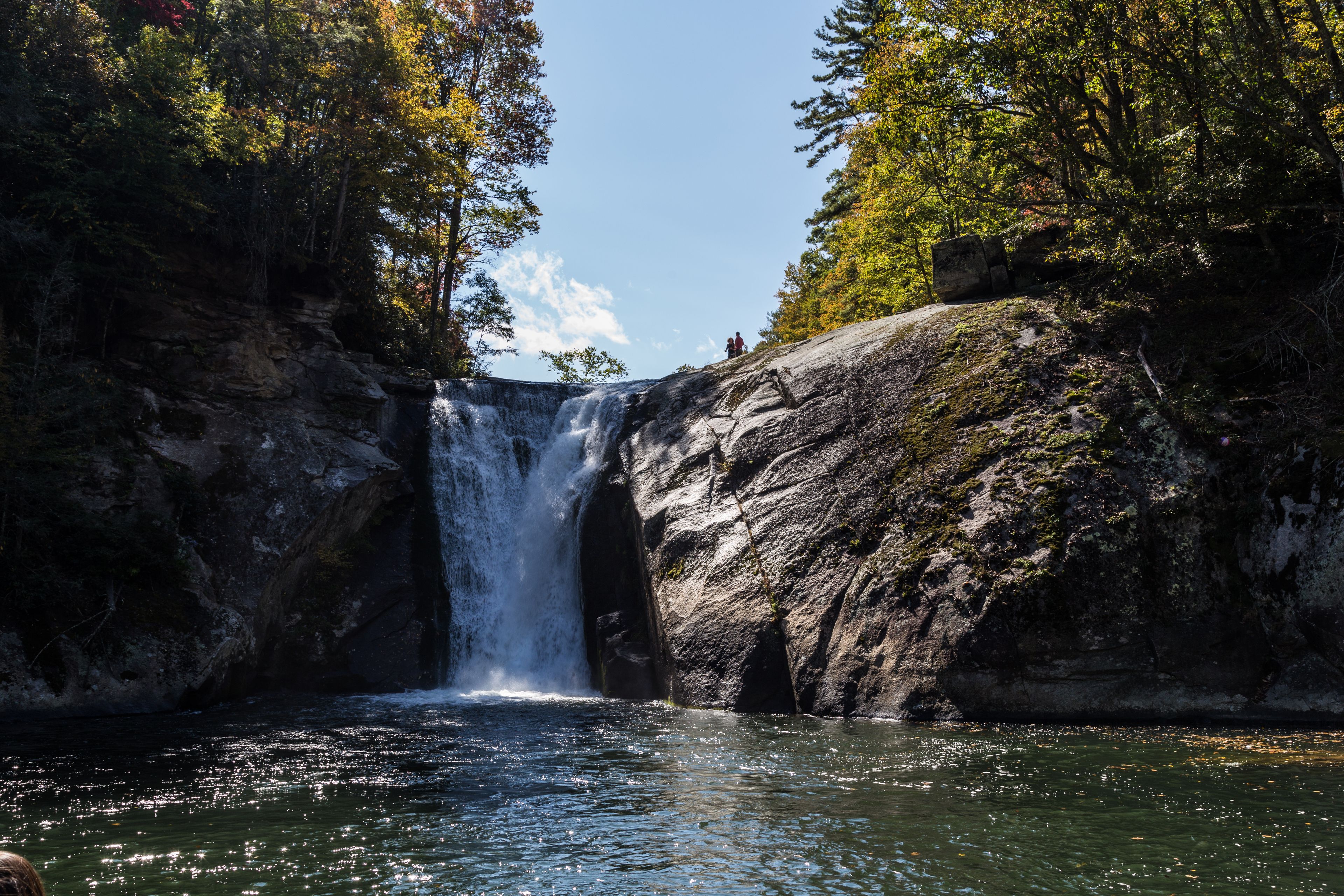 Un cascada que baixa per un penya-segat rocosos fins a una calma piscina d'aigua envoltada per arbres.