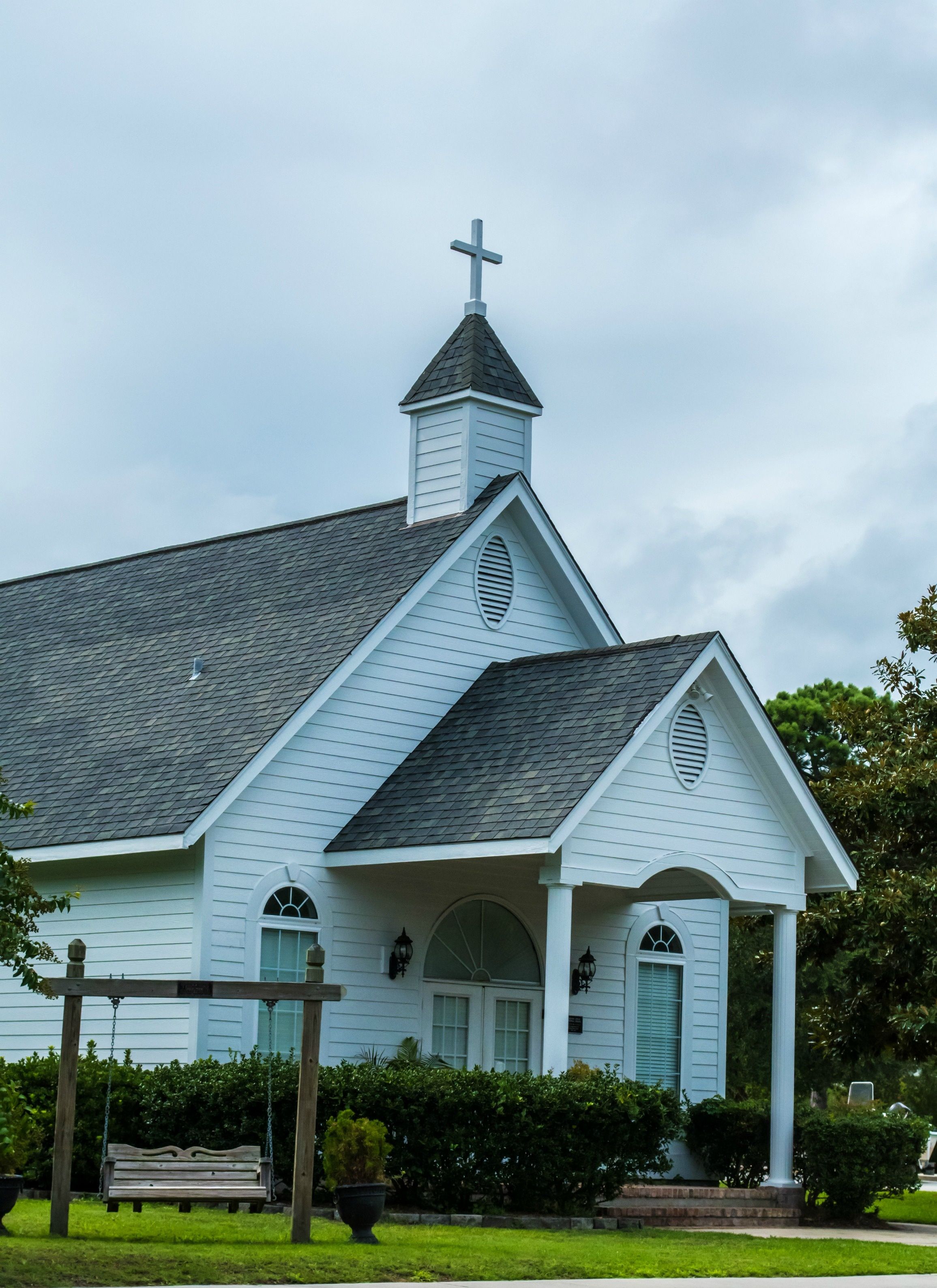 A white church with a cross on top, a steeple, and a porch with columns.