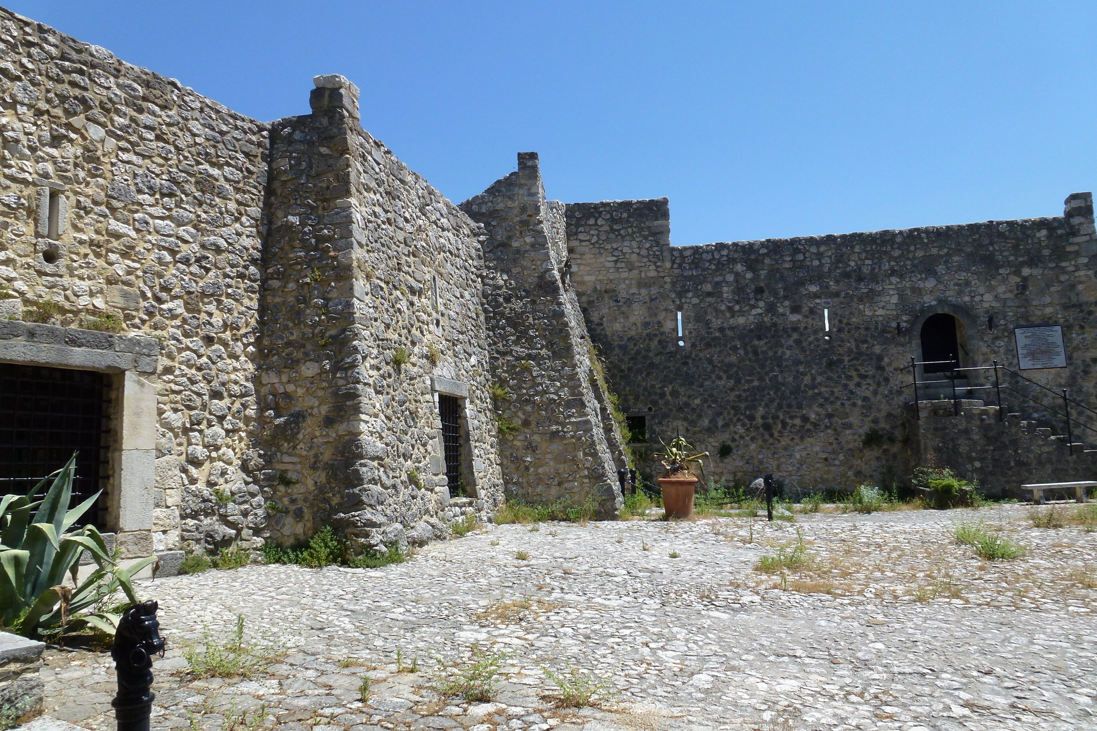 A stone building with a cobblestone courtyard, a potted plant, and a bench.