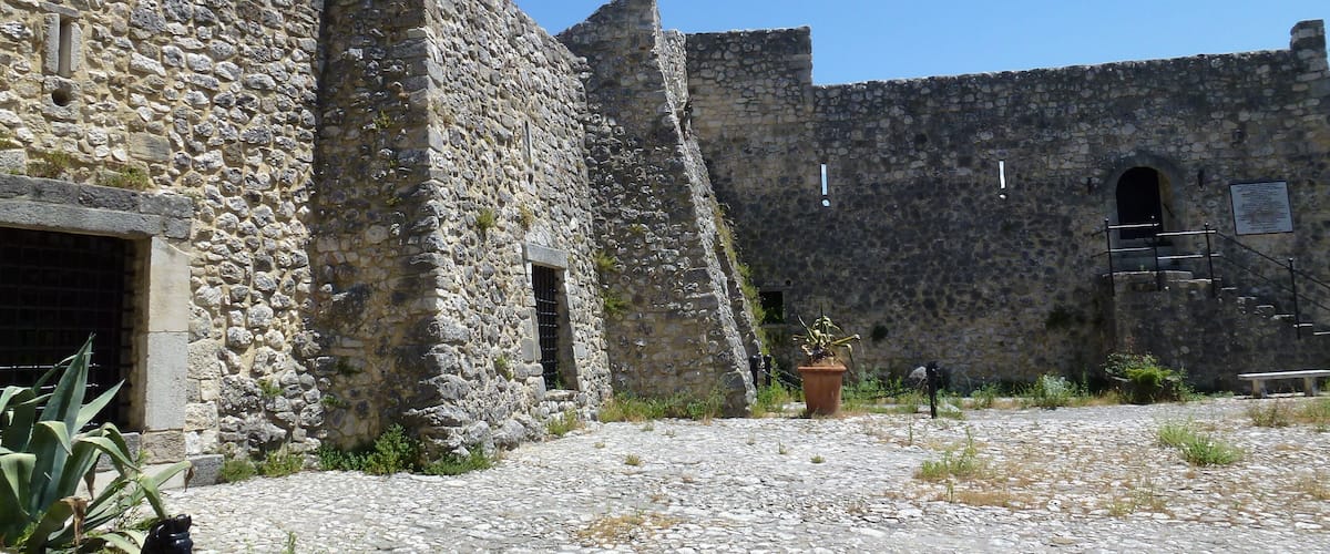 A stone building with a cobblestone courtyard, a potted plant, and a bench.