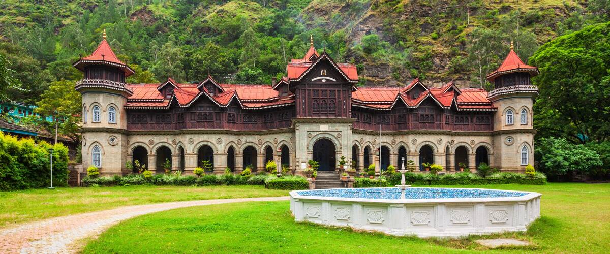 A large, ornate building with a red roof and multiple towers, surrounded by lush greenery and a paved pathway.