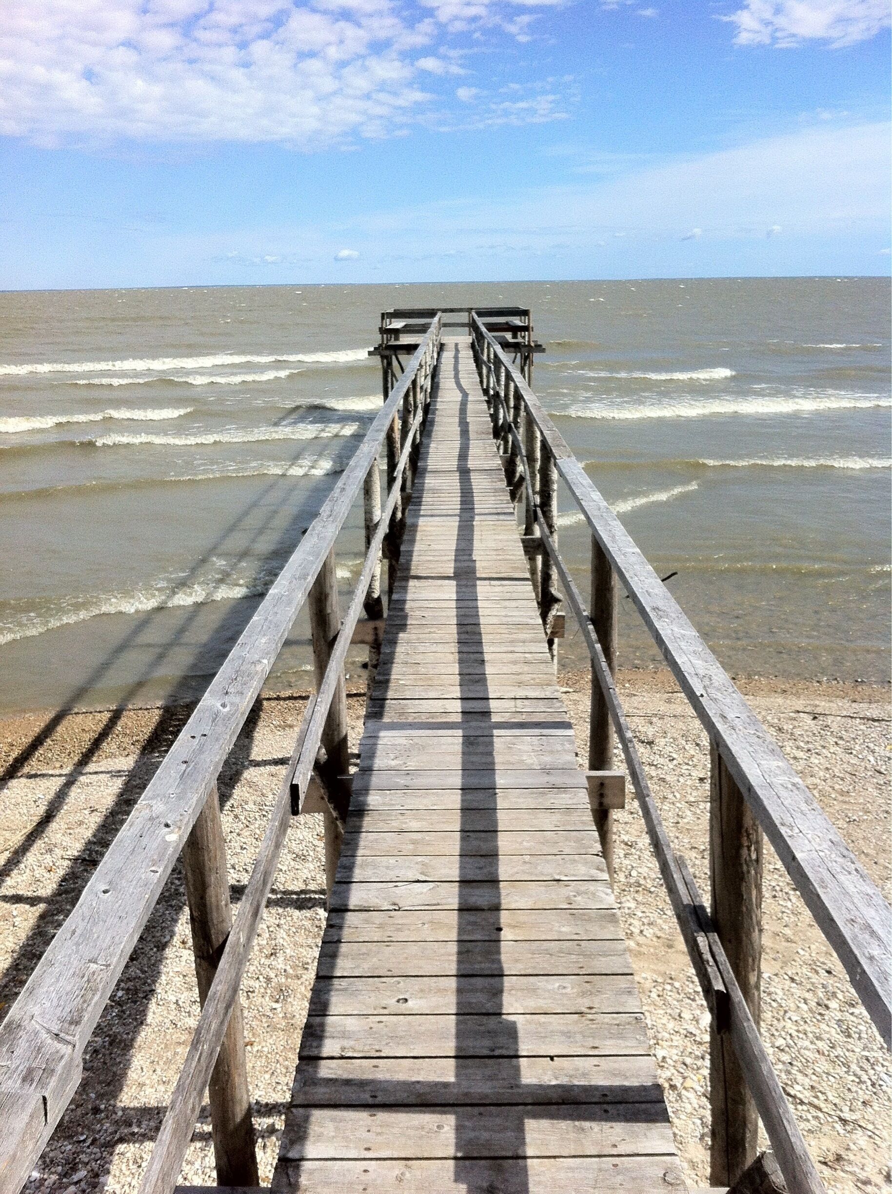 A wooden pier extending into the ocean with waves crashing at its end.
