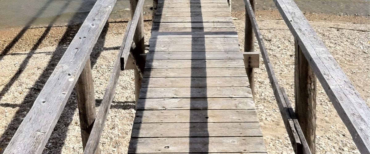 A wooden pier extending into the ocean with waves crashing at its end.