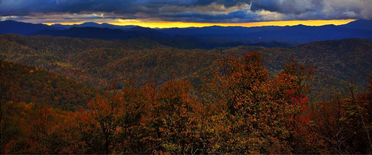A mountainous landscape with autumn foliage and a dramatic sky.