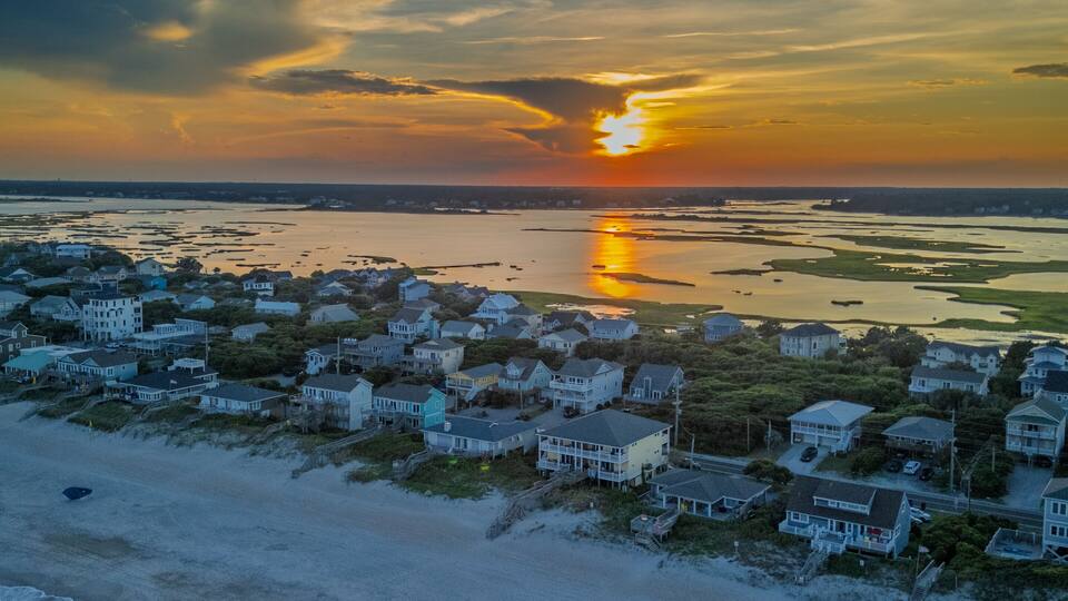 A coastal town with houses along the beach and a sunset over the water.