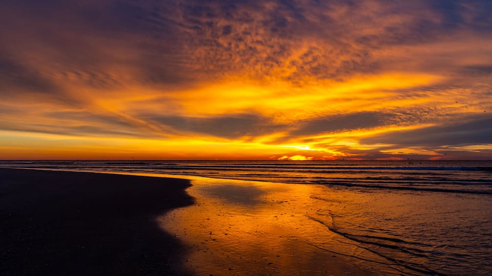 A sunset over a beach with waves and a clear sky.