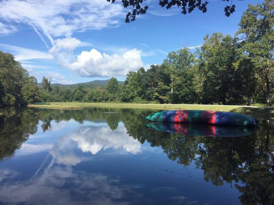 A calm lake with a green kayak floating on the water, surrounded by lush trees and a clear blue sky.