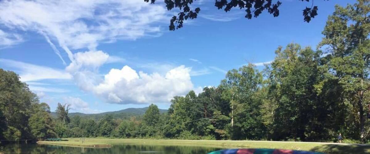 A calm lake with a green kayak floating on the water, surrounded by lush trees and a clear blue sky.