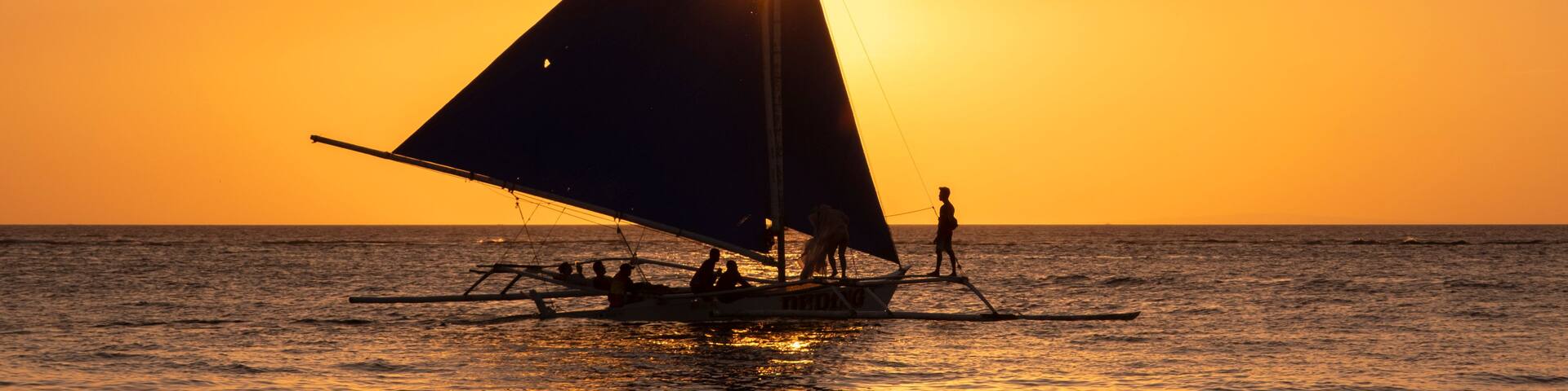 A sailboat with a large sail on the water during sunset.