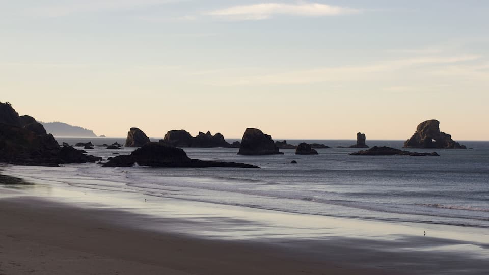 A beach with large rock formations in the water and a sandy shore.