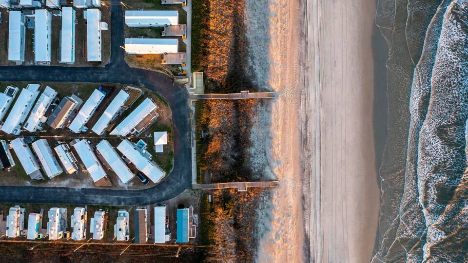 An aerial view of a coastal industrial area with warehouses, a bridge, and a beach.