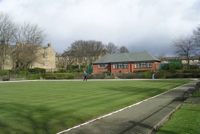 A well-maintained lawn with a paved walking path, a red building, and residential houses in the background.