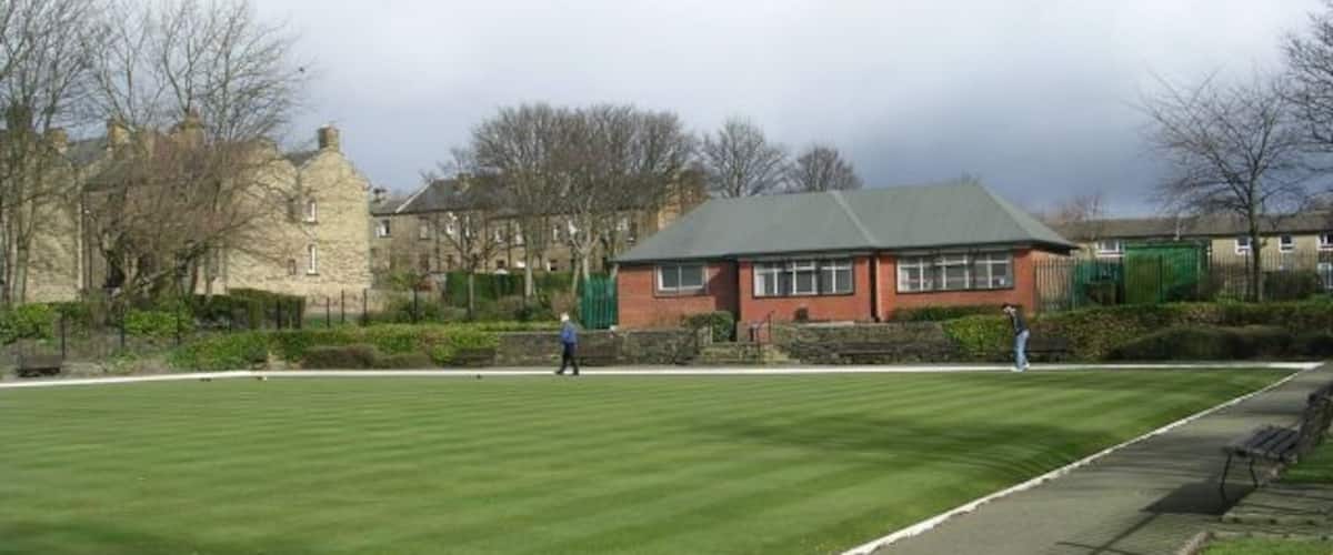 A well-maintained lawn with a paved walking path, a red building, and residential houses in the background.
