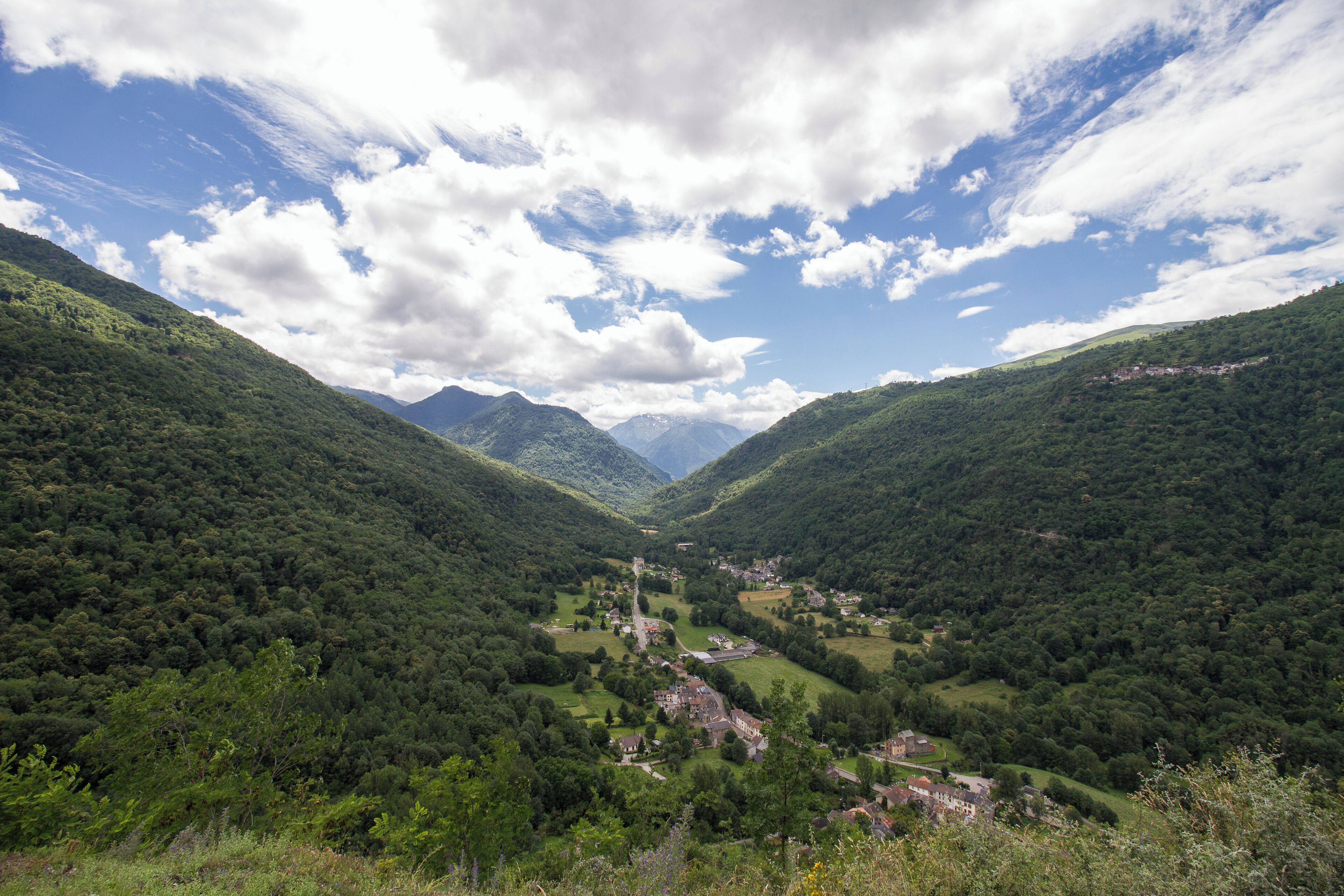 A valley with a small village surrounded by lush green hills and mountains in the background.