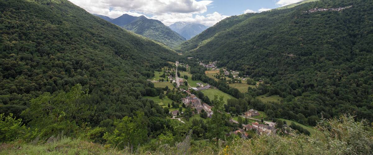 A valley with a small village surrounded by lush green hills and mountains in the background.