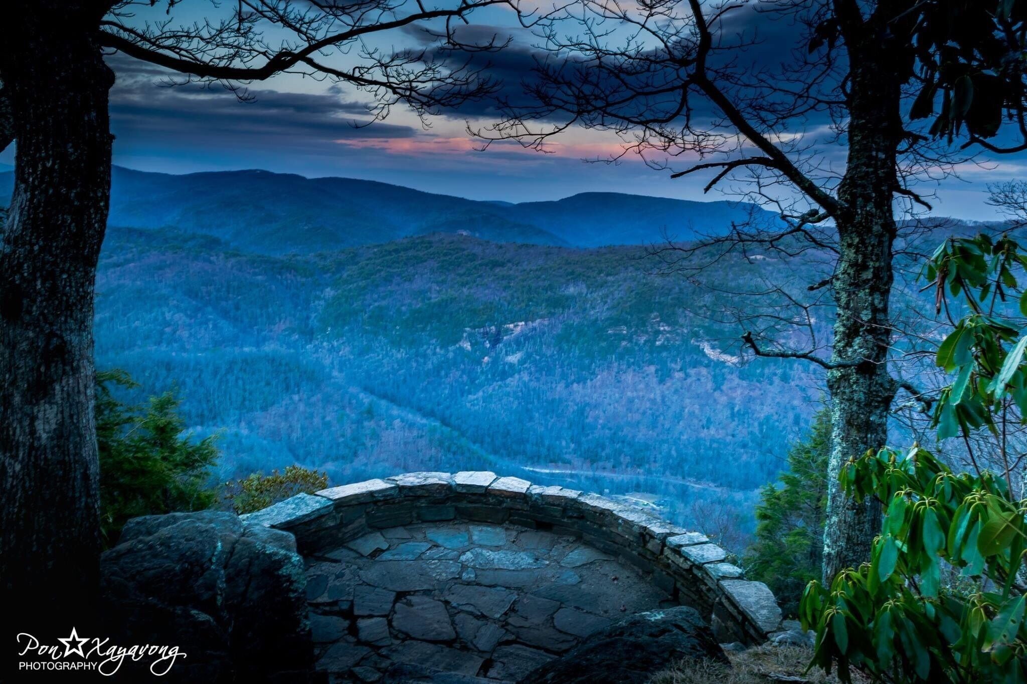 A stone bench overlooking a mountainous landscape with a view of distant hills and a cloudy sky.
